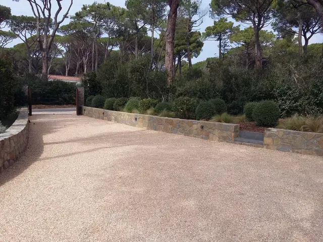 Sentiero di ghiaia vuoto, fiancheggiato da muri in pietra e alberi in un parco