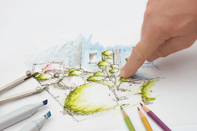 Una mano indica uno schizzo colorato di una città disegnato a mano con le matite su un tavolo bianco.