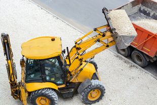 Una pala caricatrice gialla scarica ghiaia in un autocarro ribaltabile arancione in un cantiere.