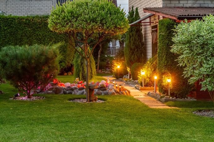Giardino sul retro, allestito con cura al crepuscolo, con un albero, un sentiero di pietra e luci soffuse.