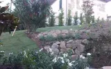 Giardino terrazzato in pietra con arbusti e fiori su un prato in pendenza