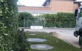 Sentiero nel cortile sul retro con pietre rotonde, siepi e una panchina bianca vicino a una casa