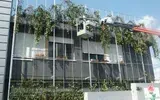 Edificio moderno con facciata in vetro, circondato da alberi e vegetazione.