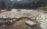 Cortile lastricato in pietra con rocce sparse e una zona di terra battuta al centro, all'aperto sotto gli alberi.