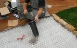 Un operaio installa un tubo di drenaggio nero sopra un tessuto geotessile bianco vicino al bordo del prato.
