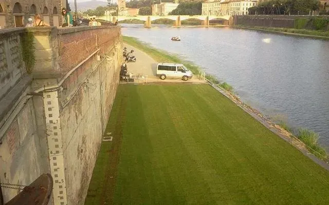 Argine fluviale con un furgone bianco parcheggiato accanto a un ampio pendio erboso e un muro di pietra sotto un ponte.