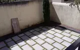 Angolo di patio pavimentato con piastrelle di pietra chiara, pareti beige e una tavola appoggiata al muro.