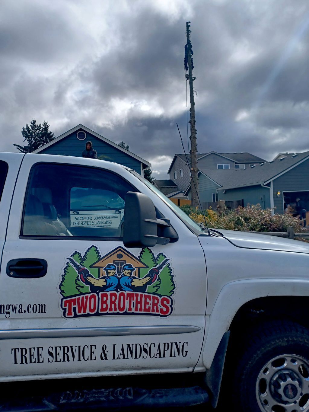 White tree service truck with “Two Brothers” logo parked outside under cloudy sky
