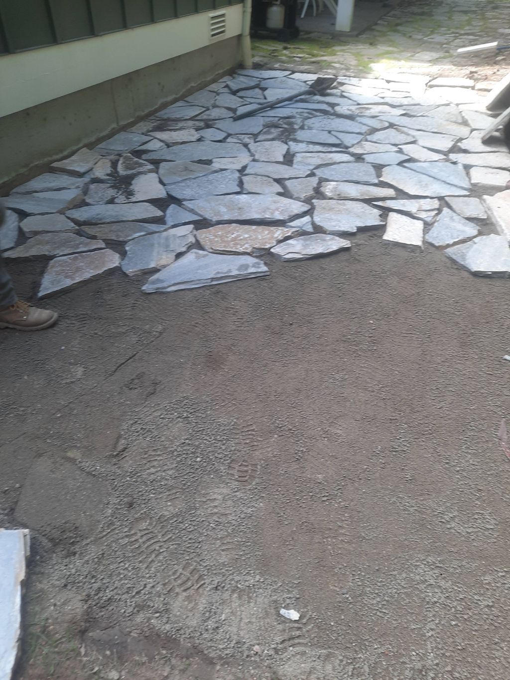 Stone-paved walkway beside a building, with a rough gravel surface in the foreground.