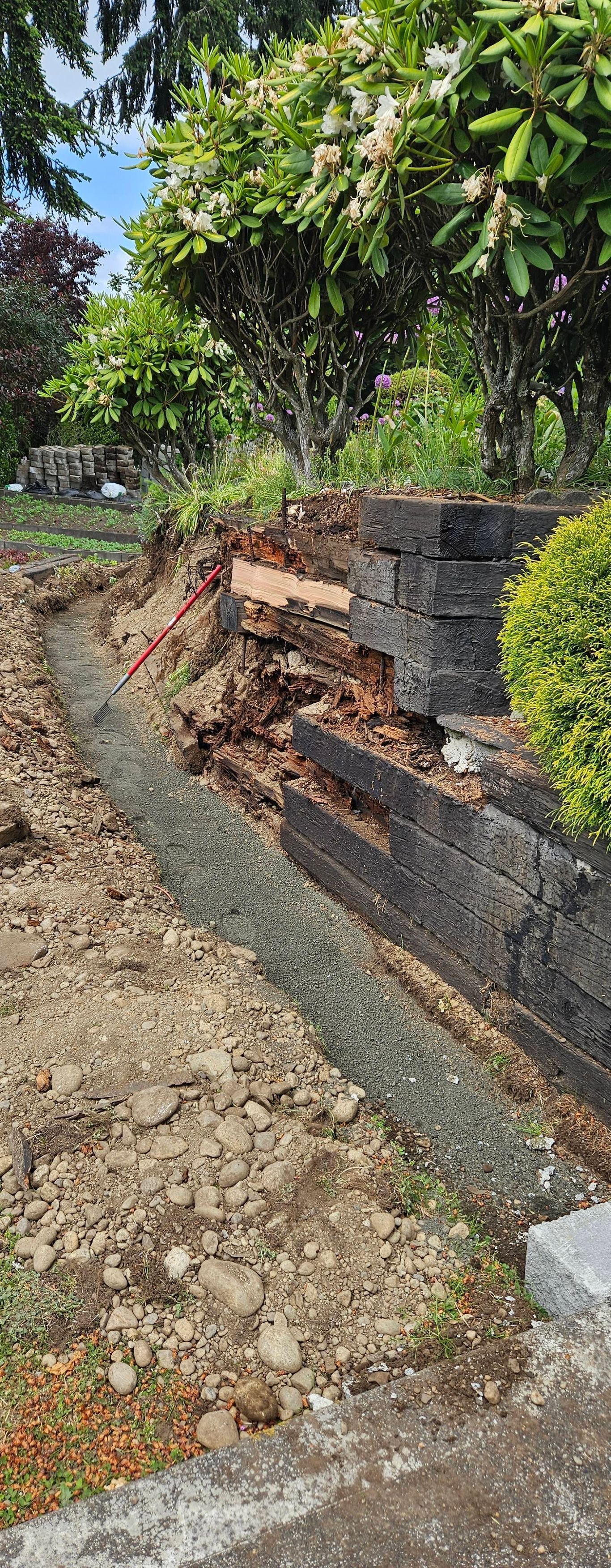 Stone retaining wall with broken steps and gravel path in a garden beneath leafy trees