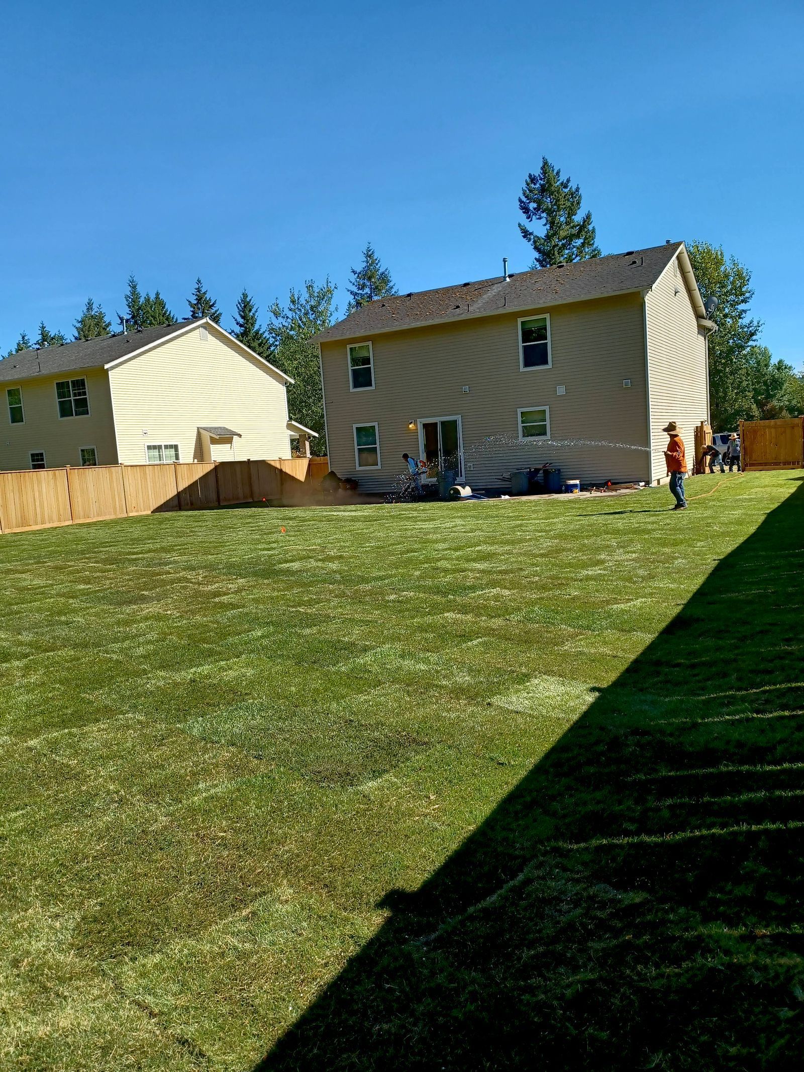 Two beige houses beside a grassy hill under a blue sky