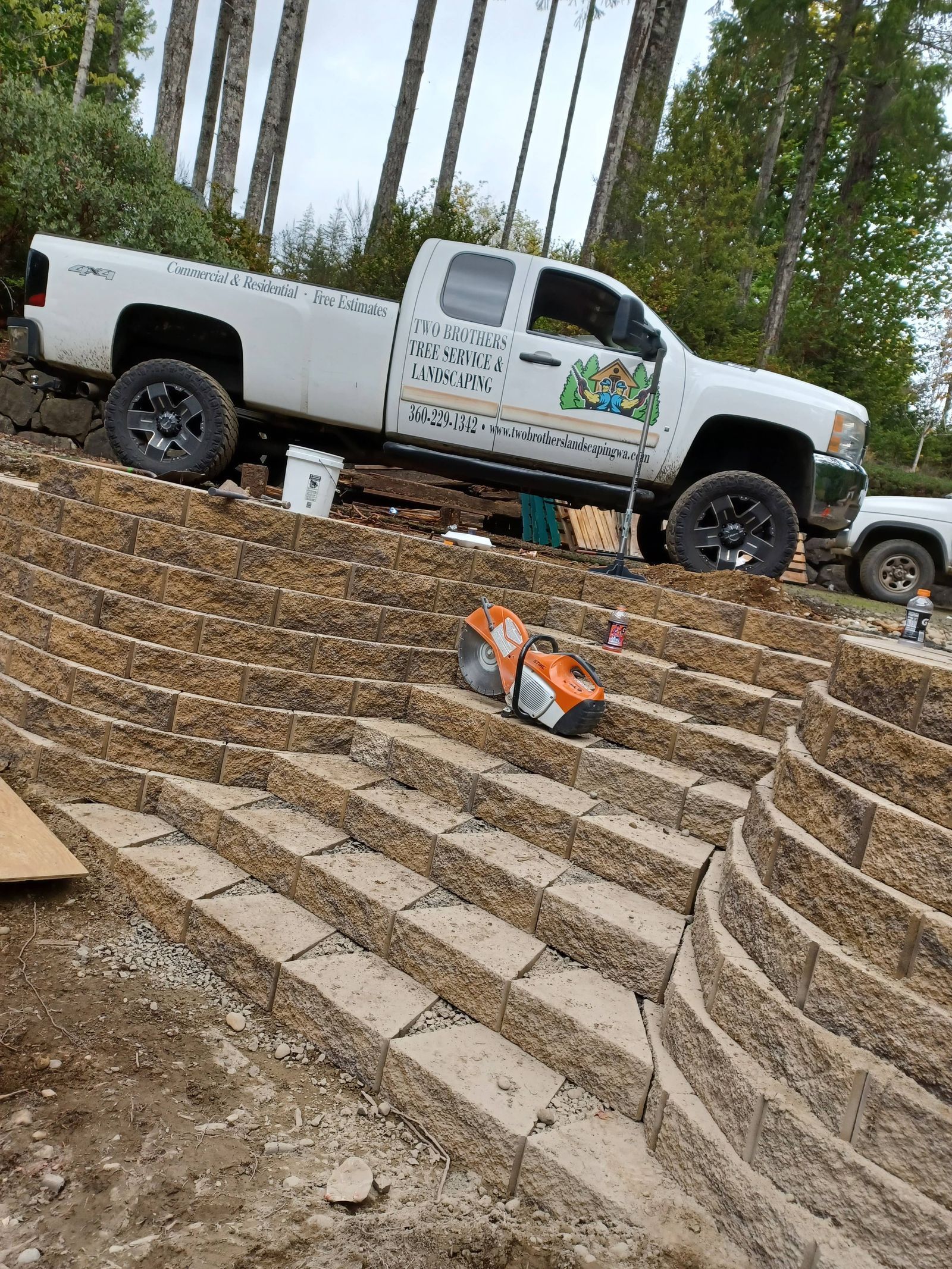White work truck parked on a dirt lot beside stone steps, with an orange tool bag in the foreground