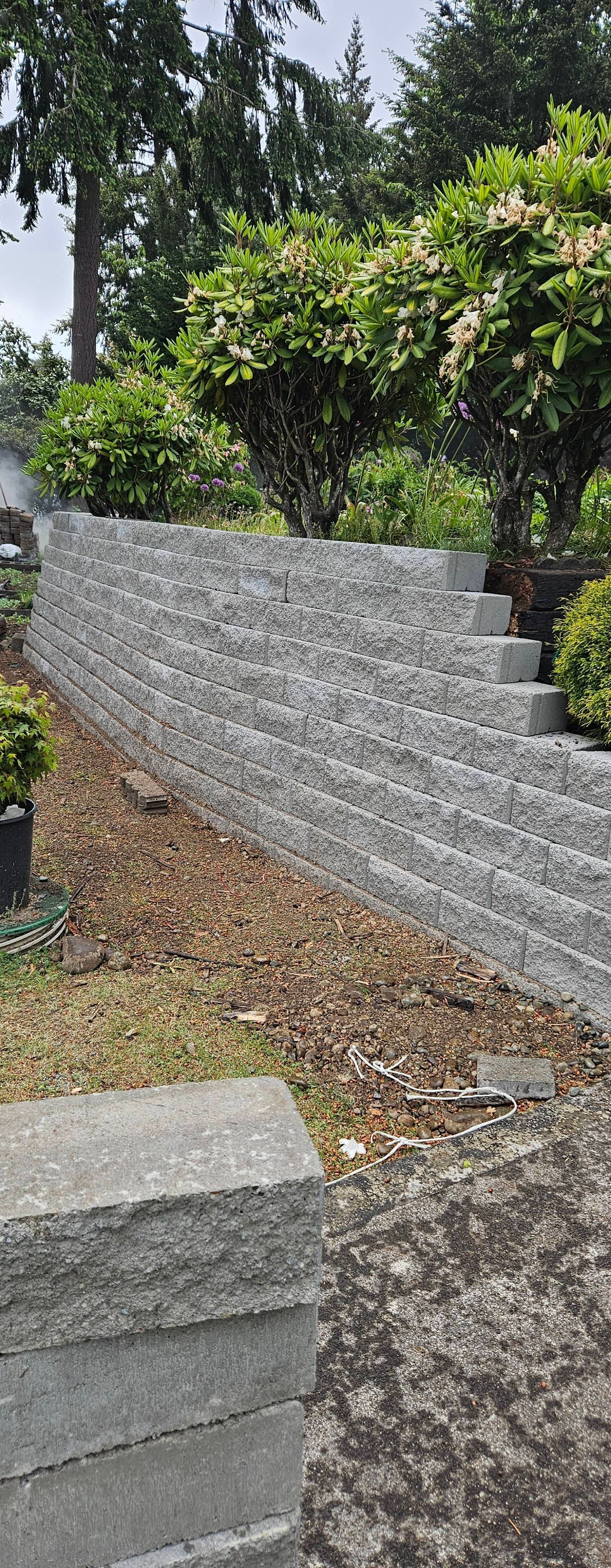 Stone retaining wall with steps beside a leafy garden and gravel path.