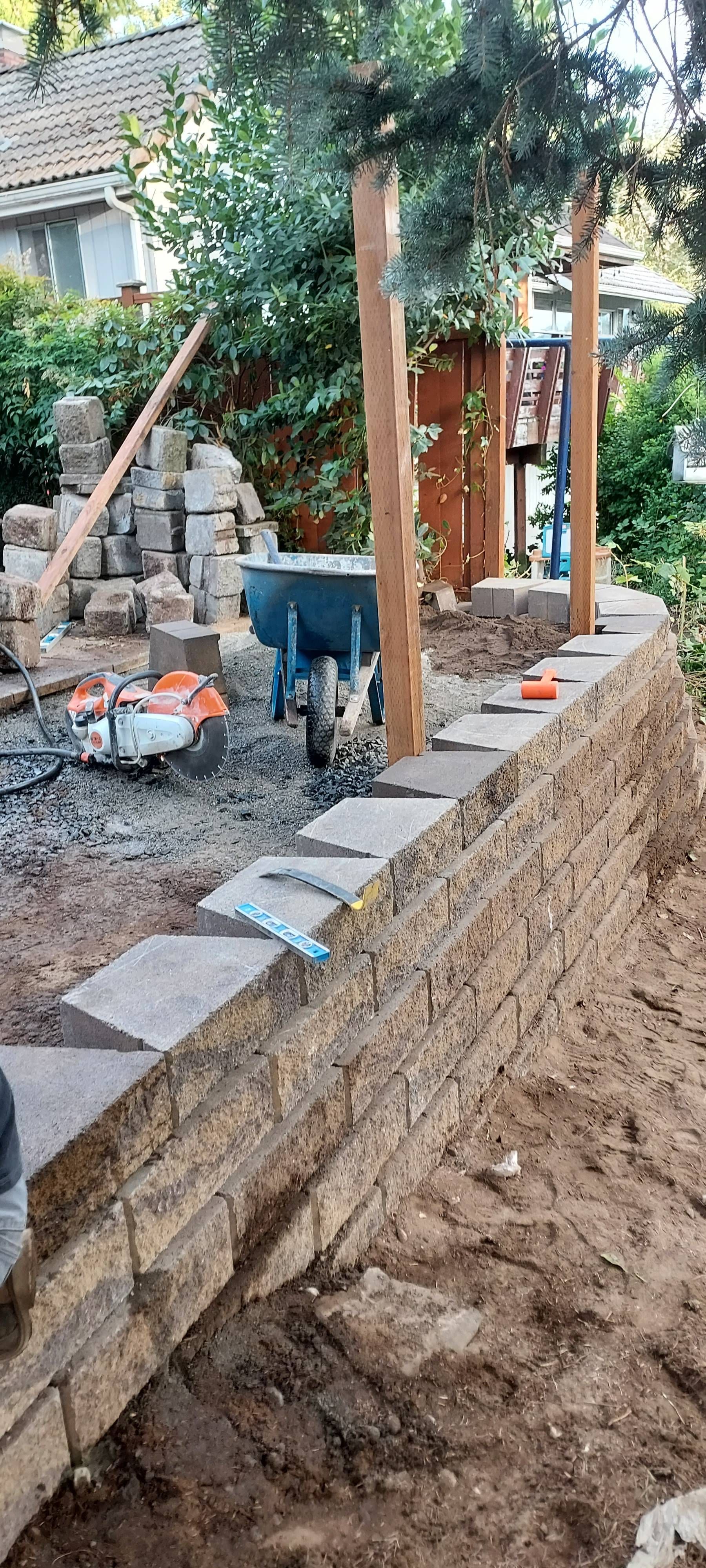 Construction site with workers, orange post forms, and a retaining wall beside a dirt excavation area