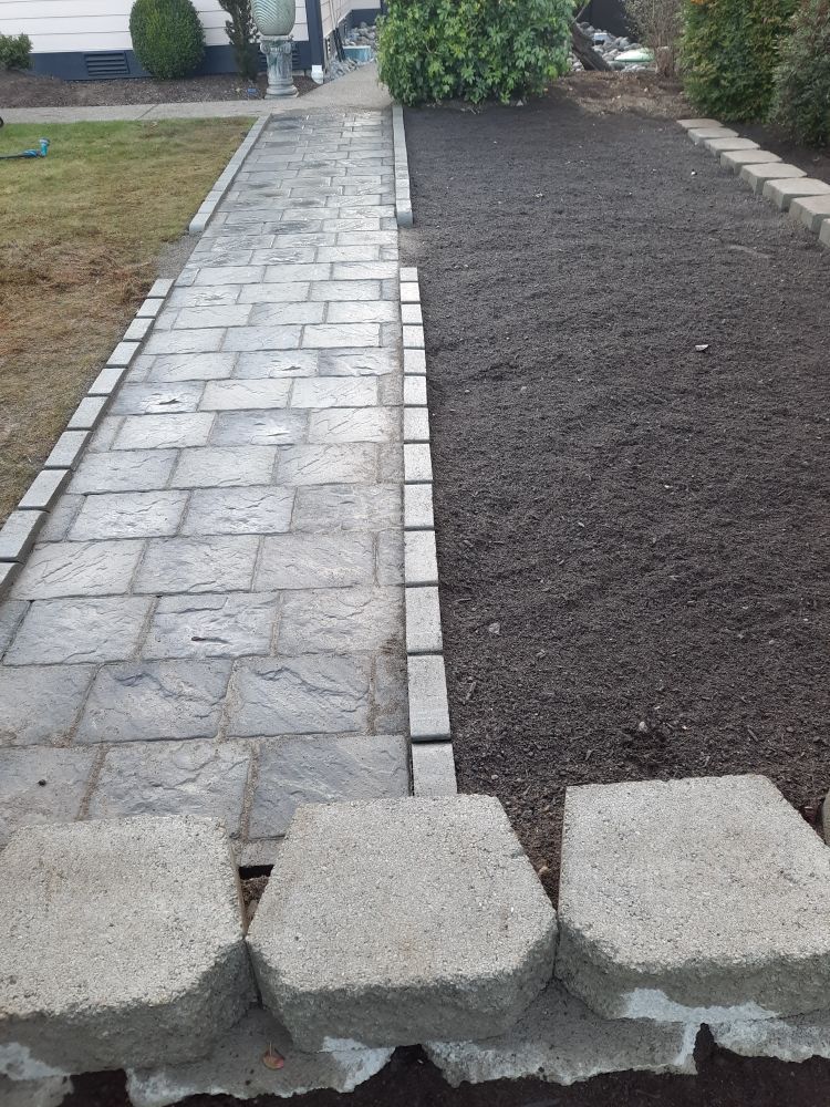 Partially paved walkway beside a dark soil path, with concrete blocks in the foreground