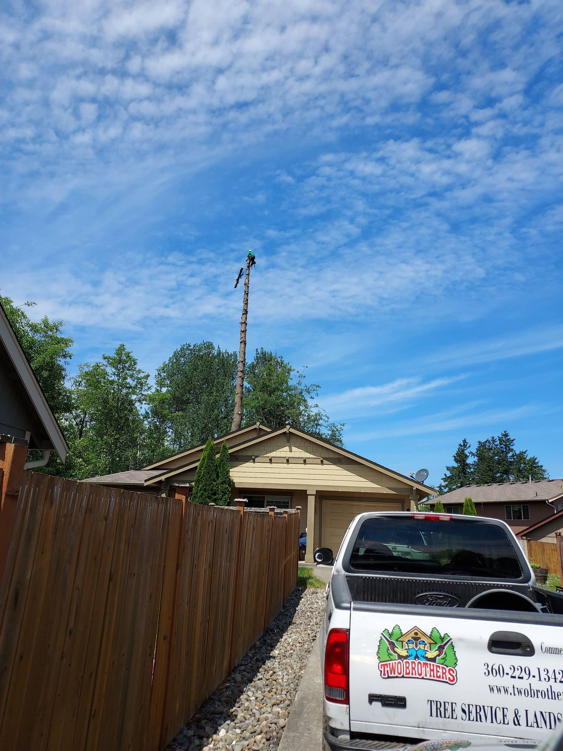 Driveway with white pickup truck, wooden fence, house carport, and blue sky with clouds.