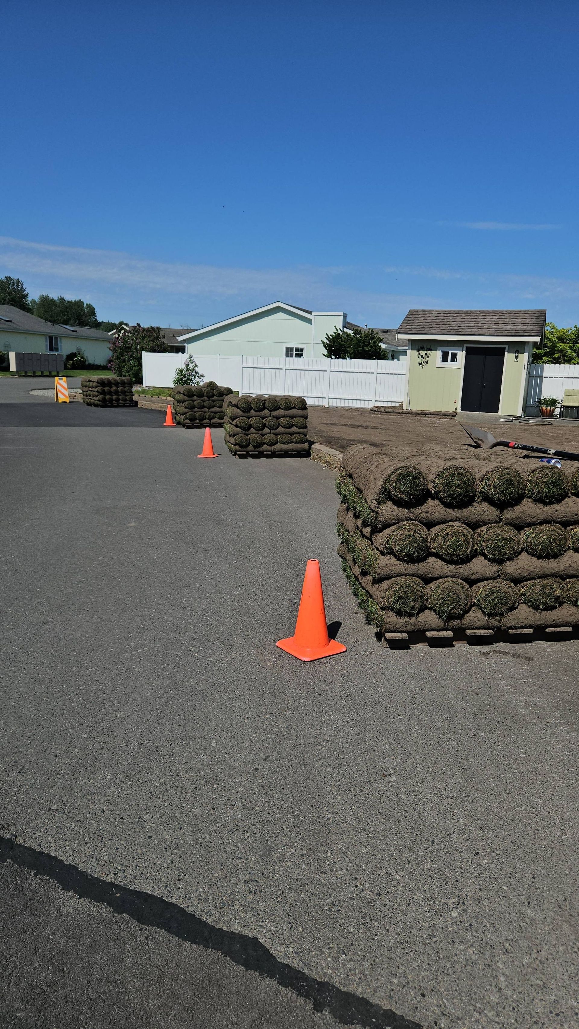 Outdoor lot with stacked pallets, orange cones, and a small white building under a clear blue sky