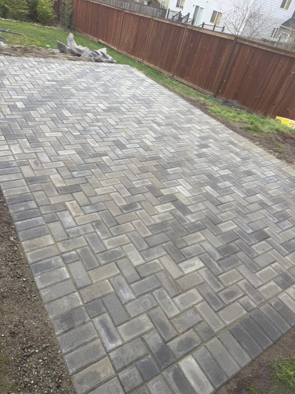 Gray stone-paver driveway beside a brown wooden fence and gravel borders.