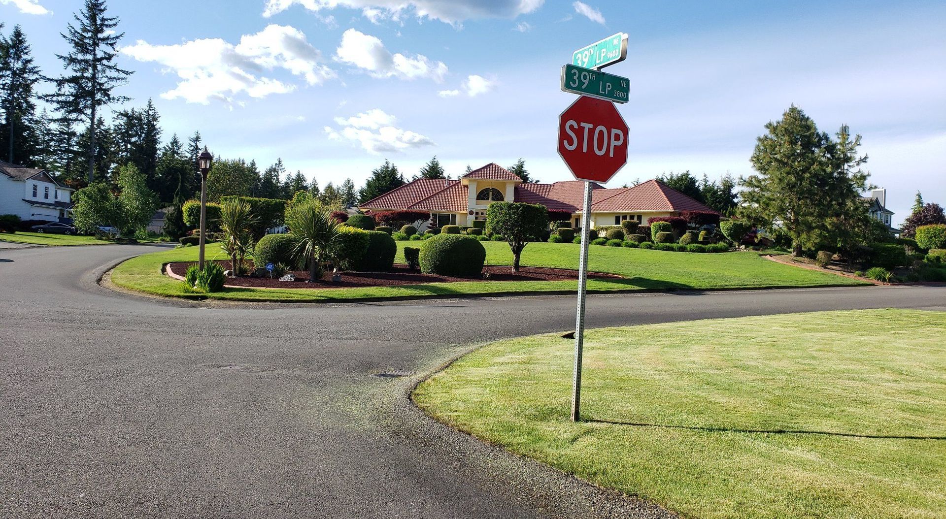 Stop sign at a curved driveway in a landscaped suburban neighborhood under a bright blue sky.