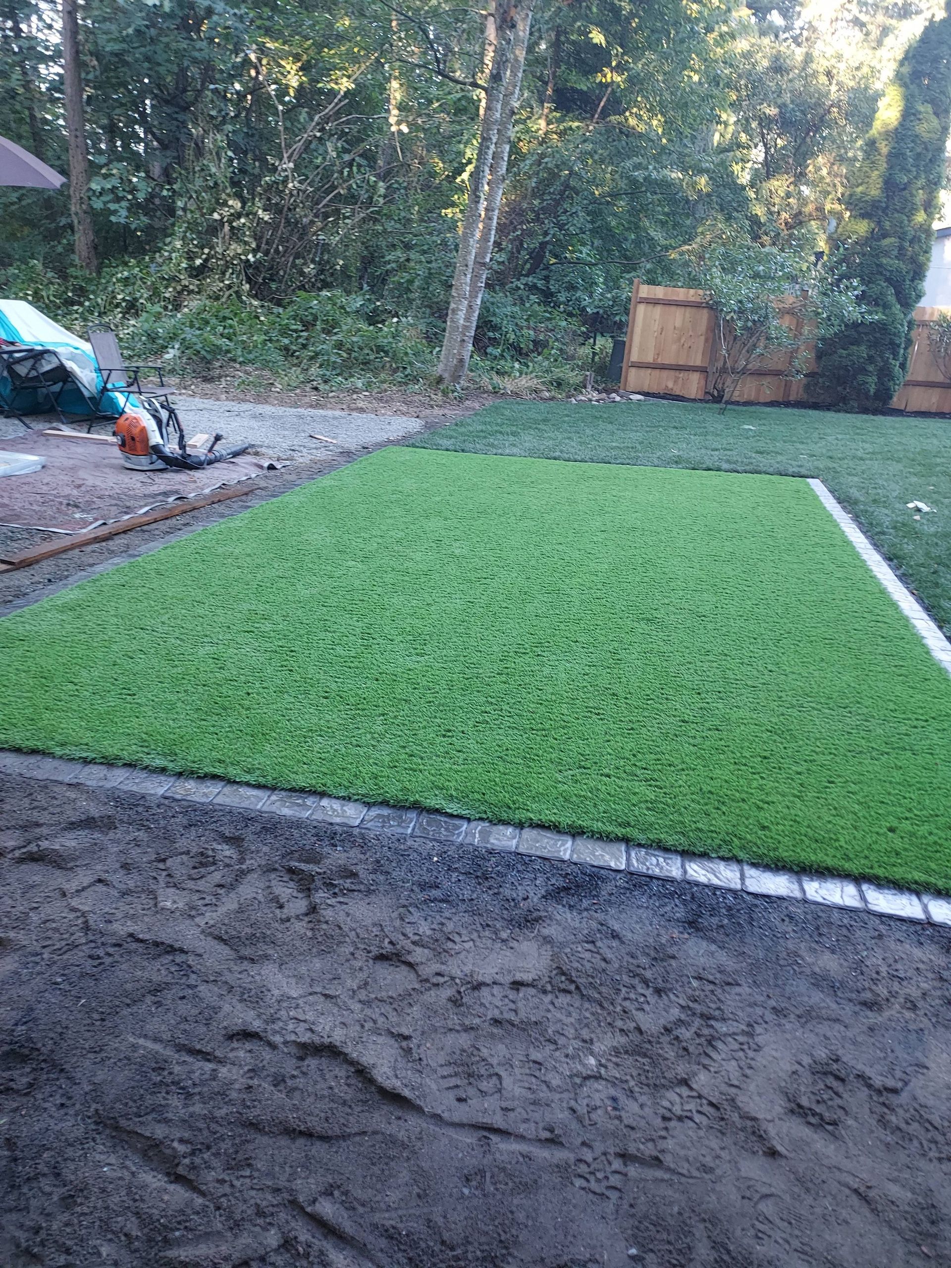 Fresh green artificial turf installed beside a gravel path in a wooded yard.