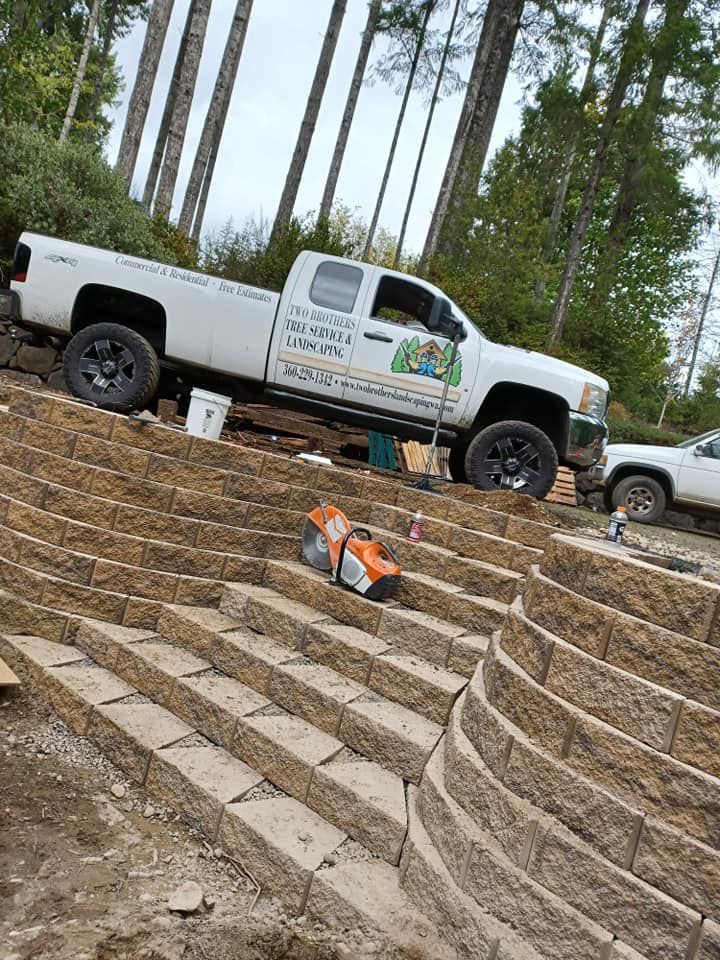 White pickup truck parked on stone steps beside a dirt path, with orange traffic cones in front and trees behind