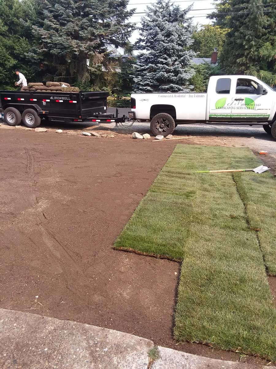 A truck is parked in a driveway next to a trailer filled with grass.