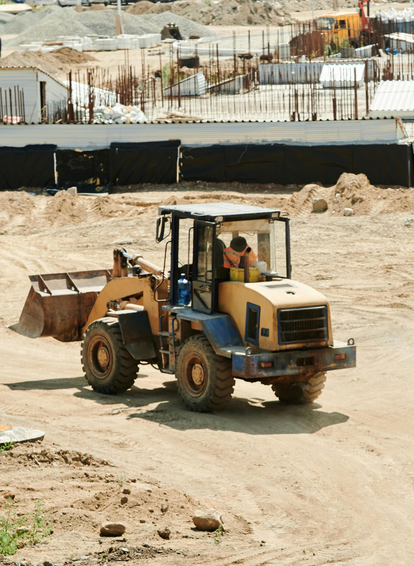 Three construction workers reviewing blueprints on a table at a construction site. They wear orange vests and hard hats.