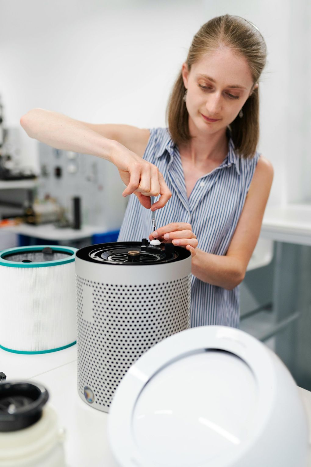 A person uses a small tool to adjust the top of a cylindrical air purifier on a workbench.