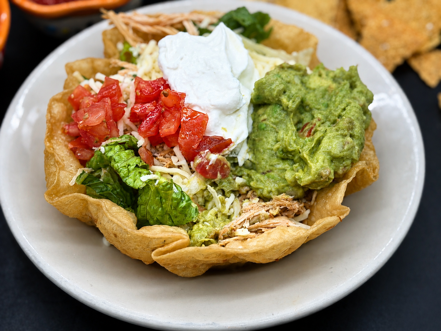 Mexican tostada topped with guacamole, sour cream, diced tomatoes, and shredded chicken on a white plate