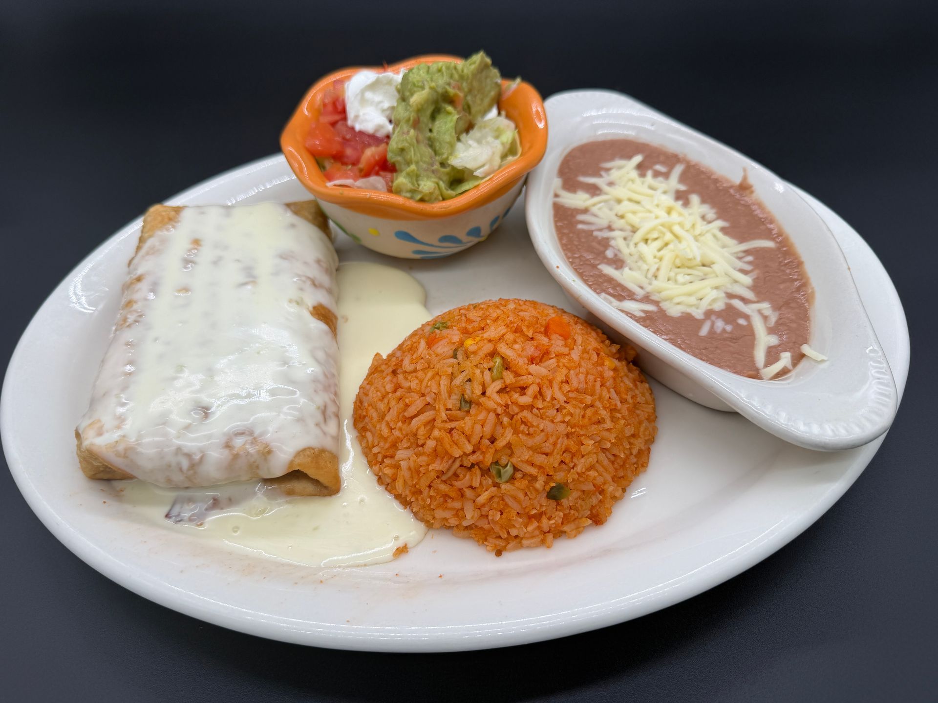 Plate with burrito, rice, refried beans, and a small salad on a white dish
