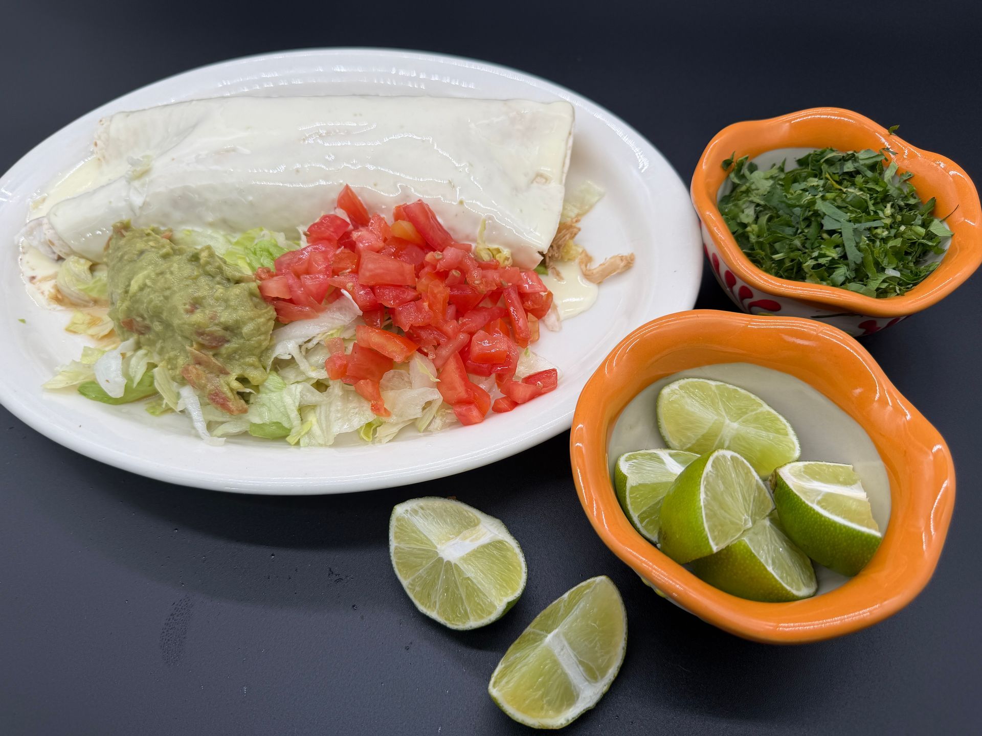 Tacos with shredded lettuce, diced tomatoes, lime wedges, and green salsa on plates and bowls