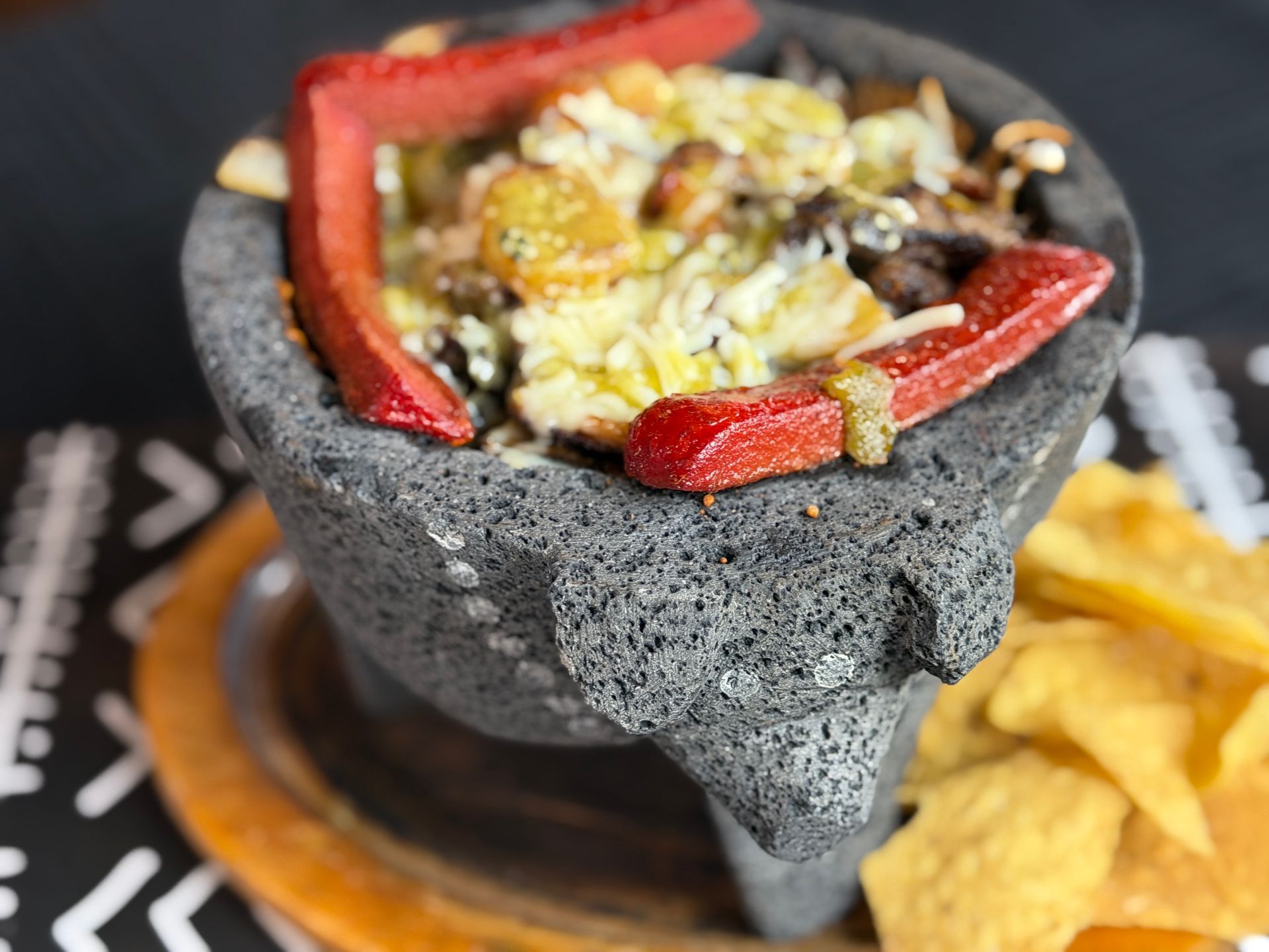 Molcajete with melted cheese, roasted vegetables, and tortilla chips on a table