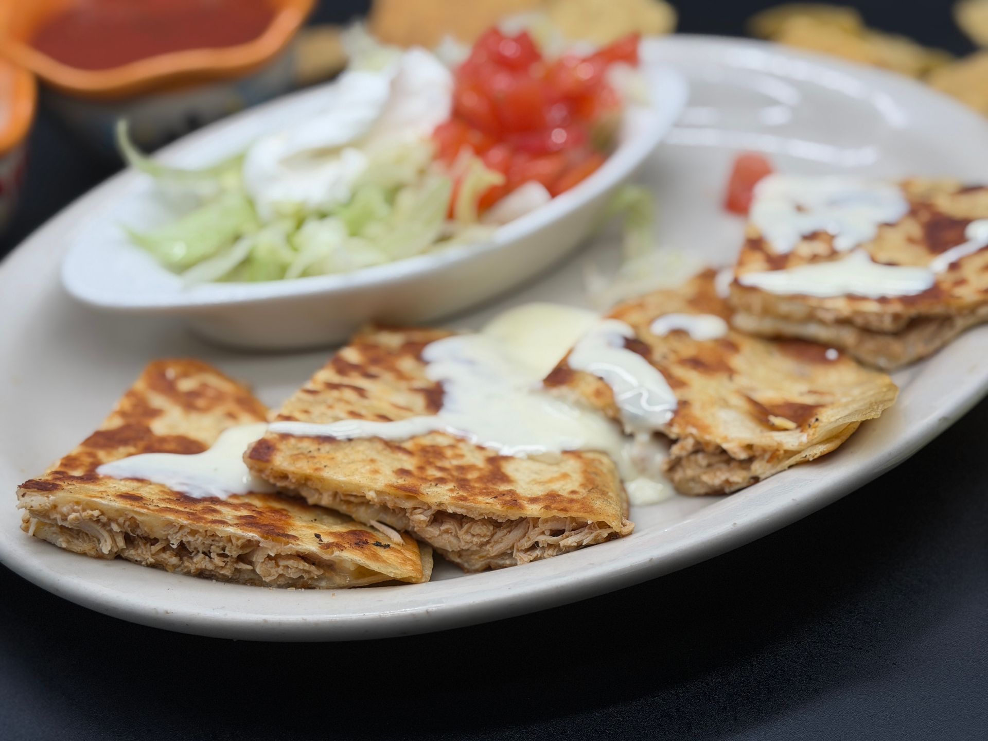 Plate of cheesy quesadilla slices with salsa and lettuce garnish on a restaurant table