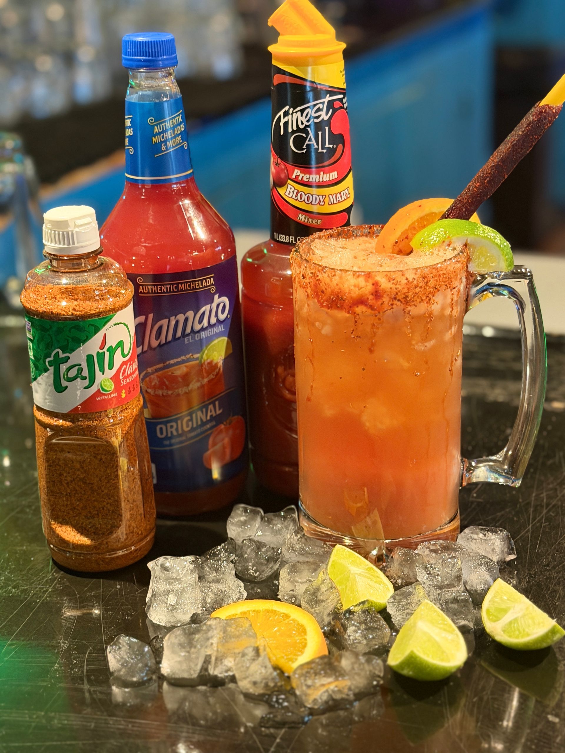 Spicy michelada in a glass with chamoy bottles and lime wedges on a bar counter.