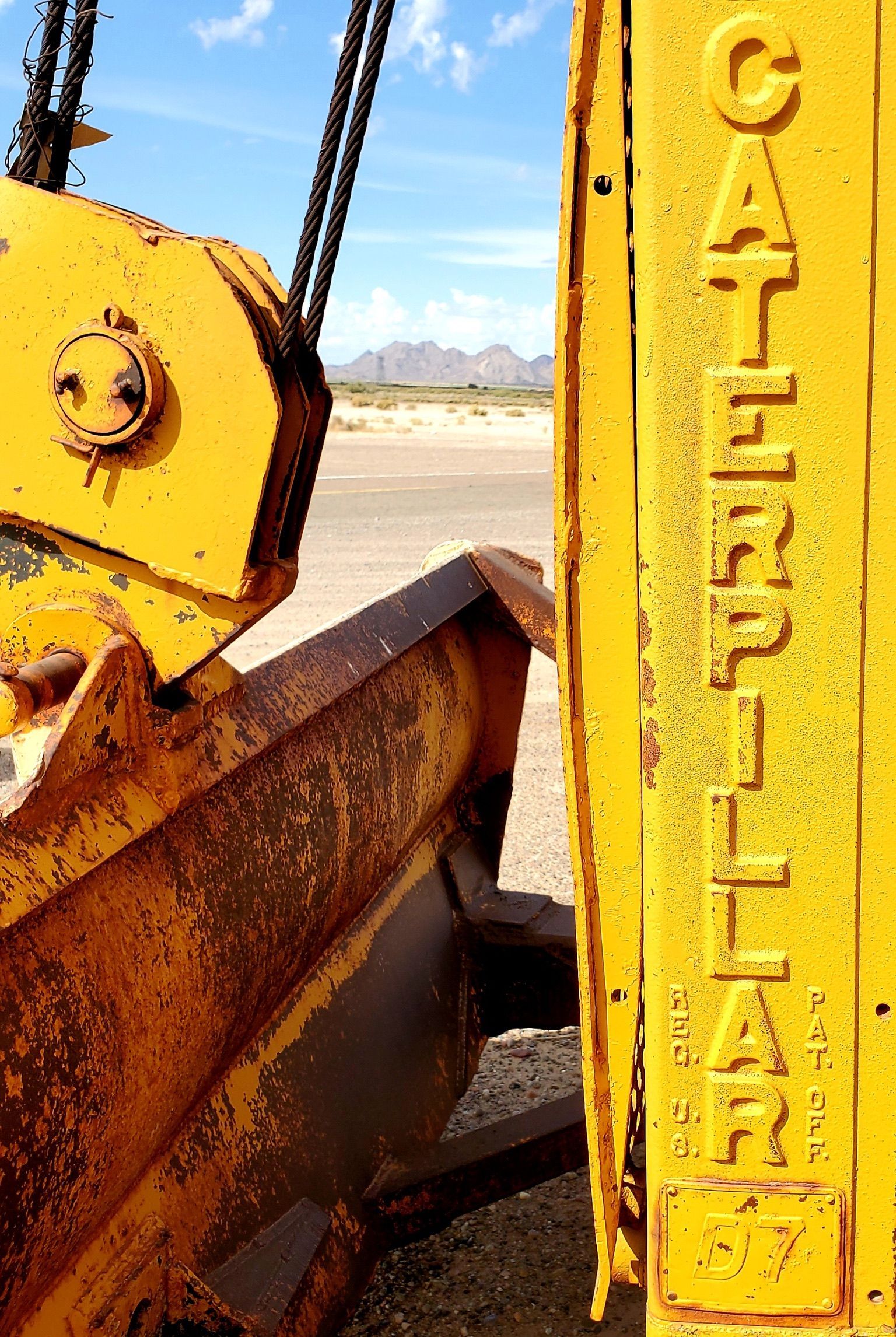 Yellow Caterpillar bulldozer with rusty parts, blue sky, and mountains in background.