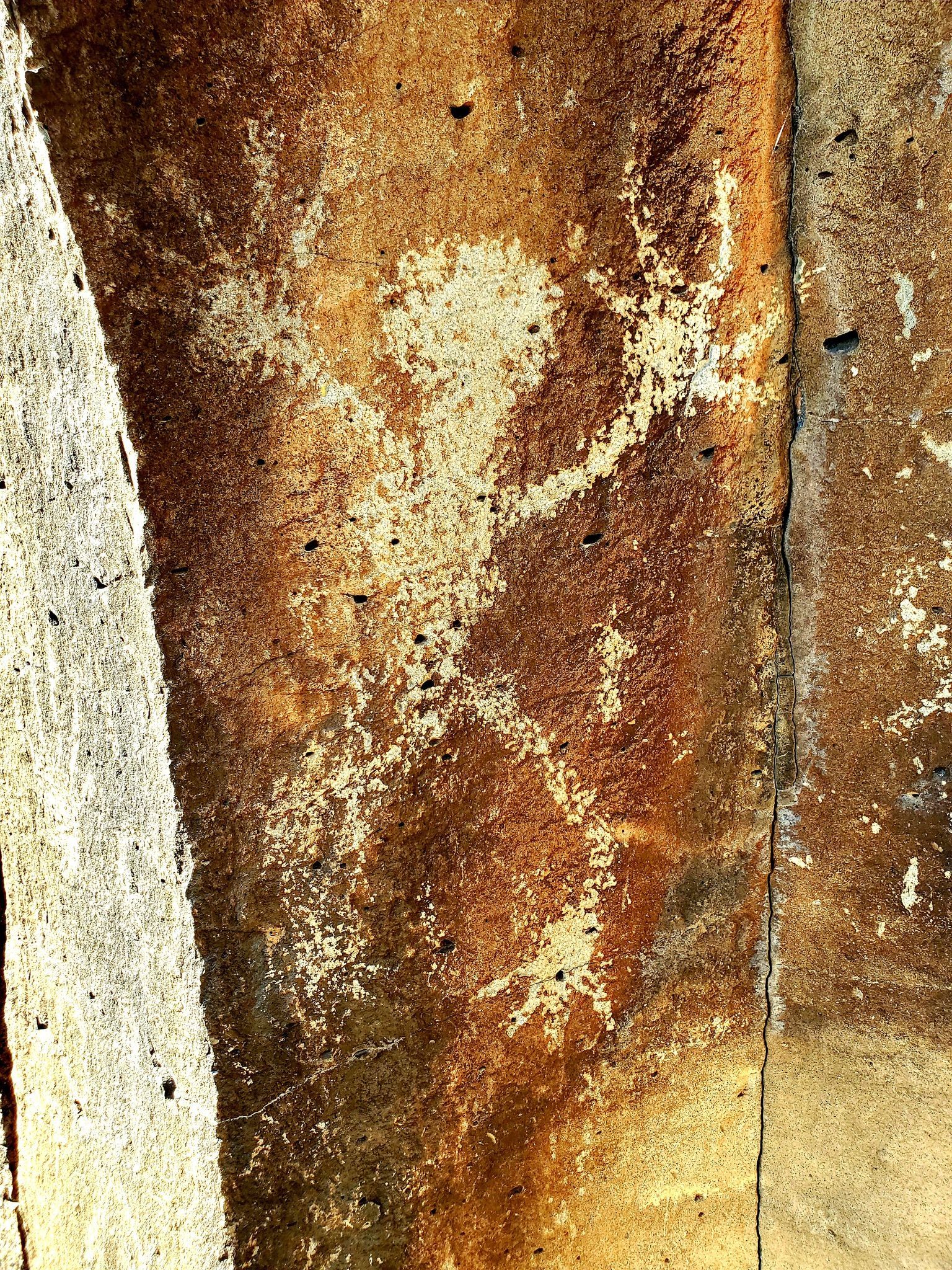 Weathered wall with peeling paint, showing brown, beige, and white colors, and a faded figure.