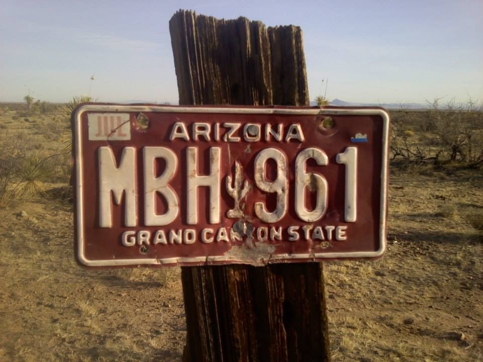 Arizona license plate MBH 961 nailed to a weathered wooden post in a desert landscape.