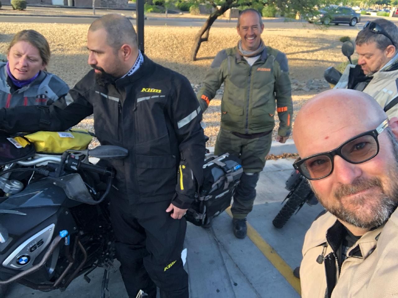 Group of motorcyclists, some in riding gear, posing near their bikes, outdoors.