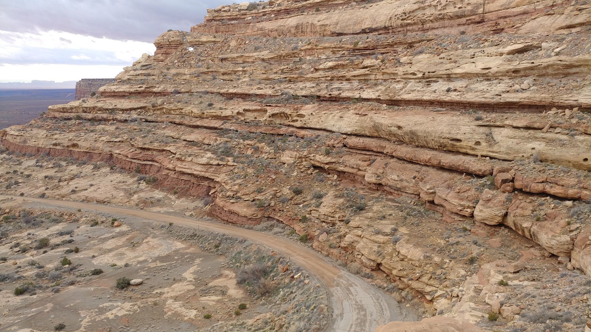 Layered sandstone cliff face with a dirt road winding along its base.