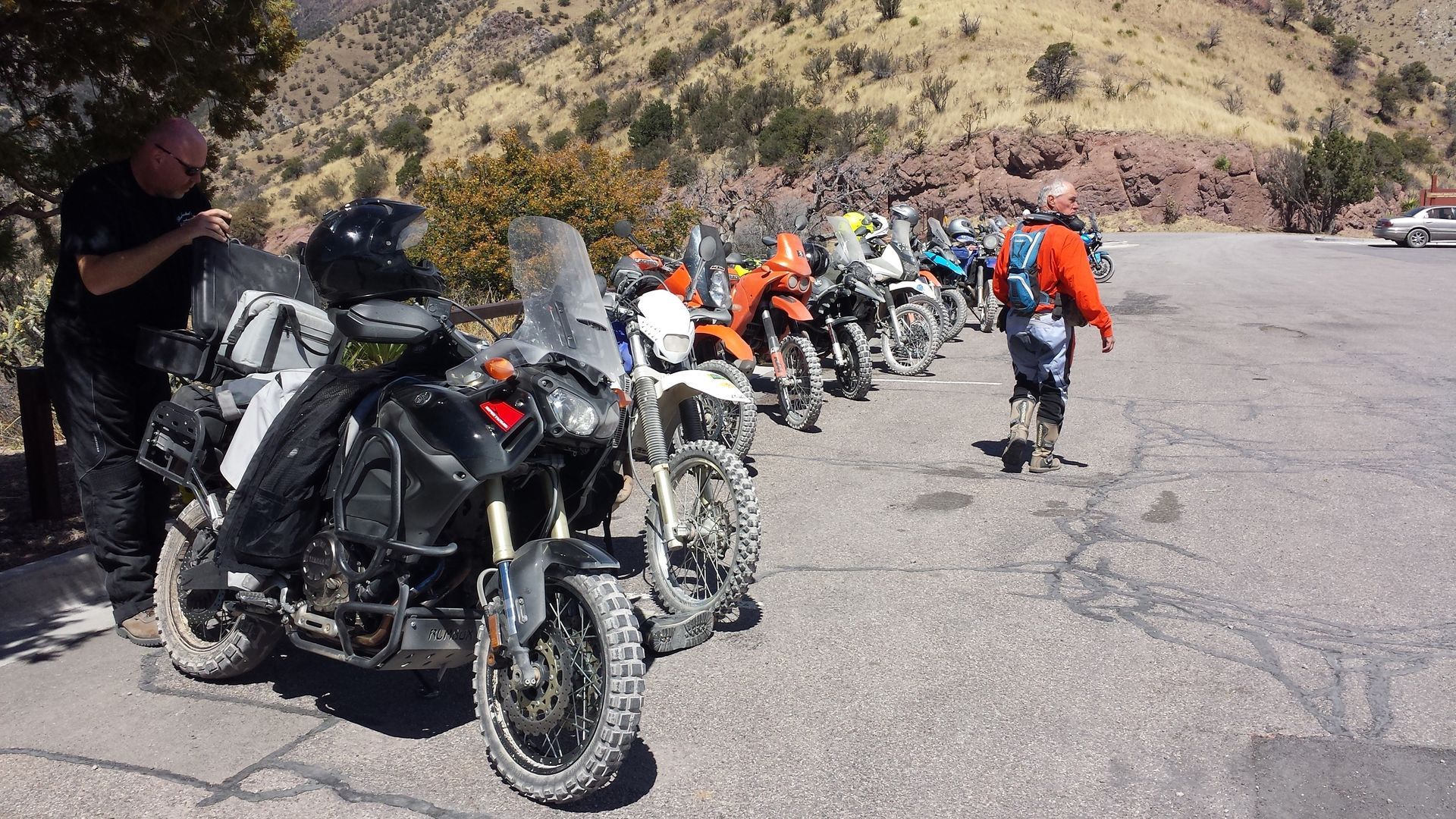 Motorcyclists in riding gear beside parked bikes on a mountain road.