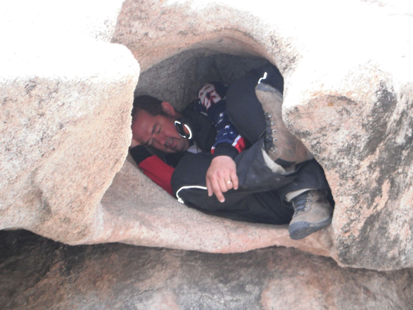Man curled up inside a rock formation, wearing dark clothing. Beige rock walls.