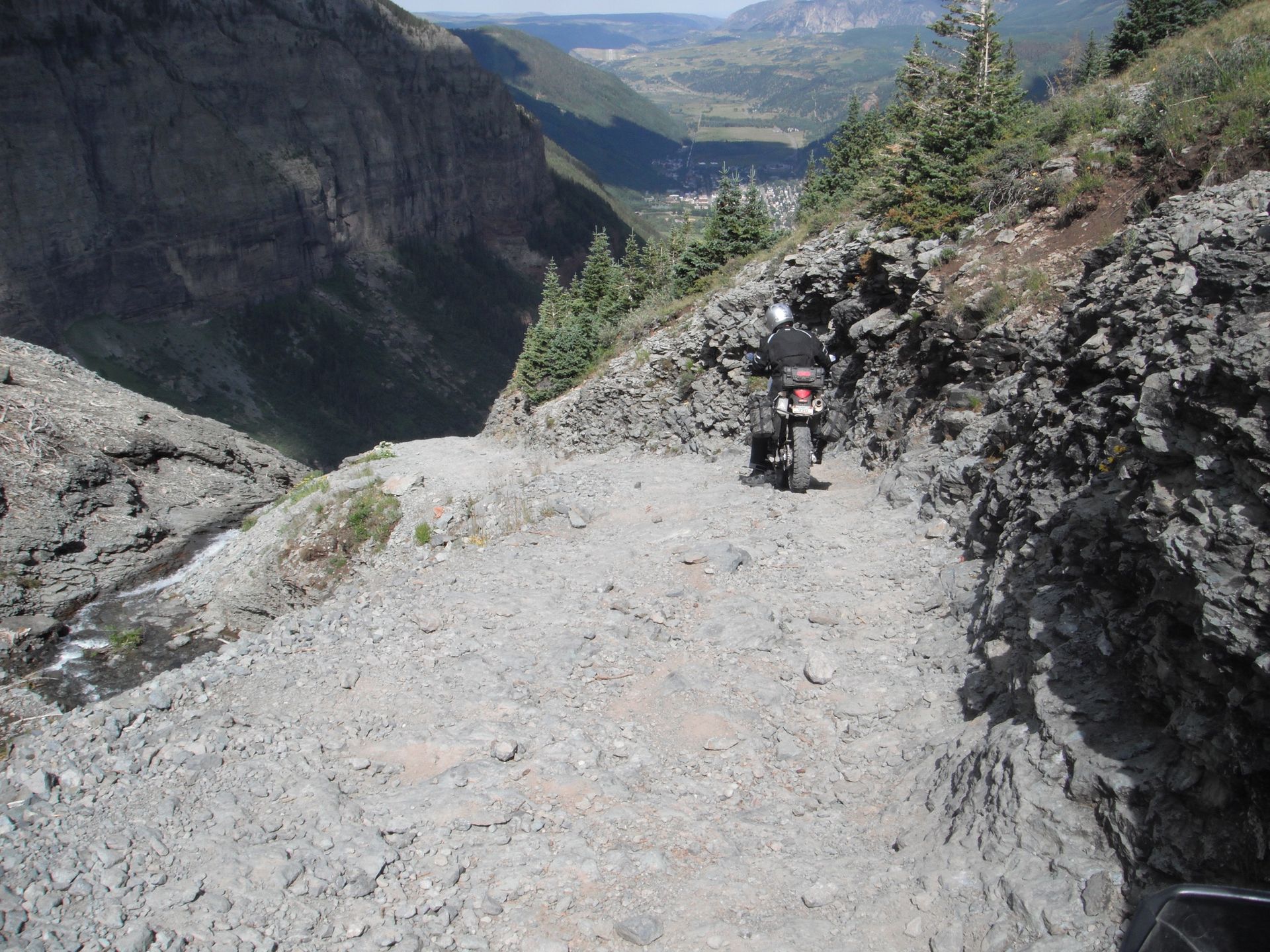 Motorcycle on a narrow, rocky mountain trail with a steep drop-off. Valley in the distance.