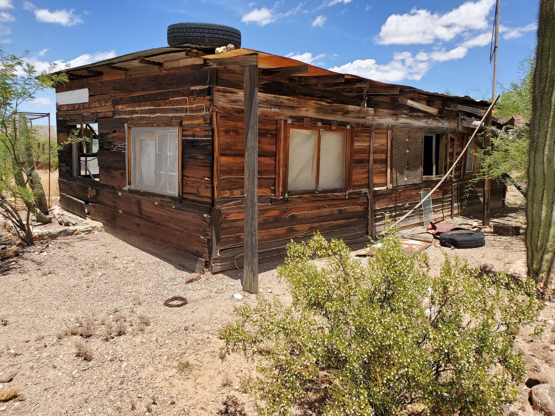 Dilapidated wooden cabin in a dry, desert environment with a tire on the roof.