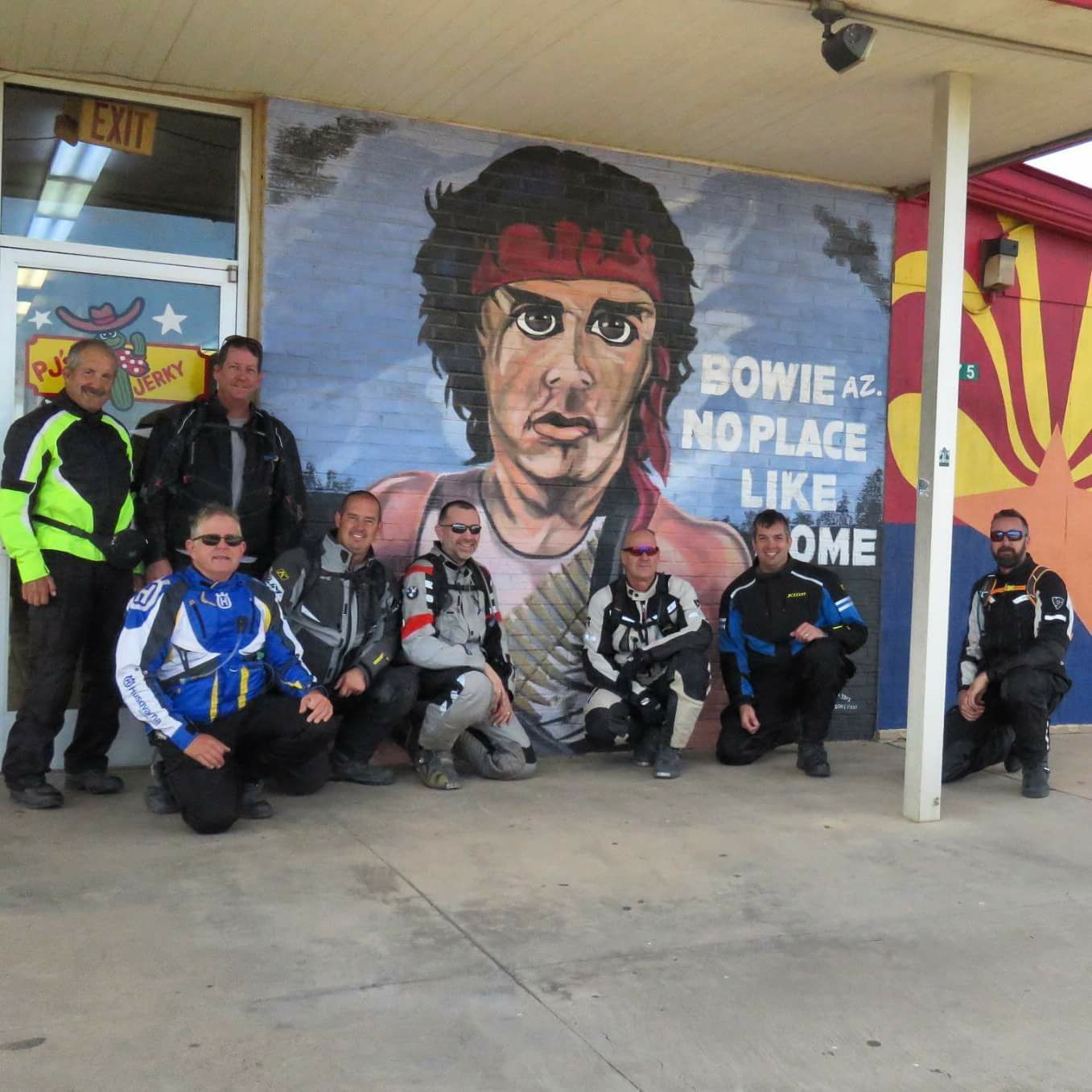 Group of motorcyclists pose in front of a mural of Sylvester Stallone in Bowie, Arizona.