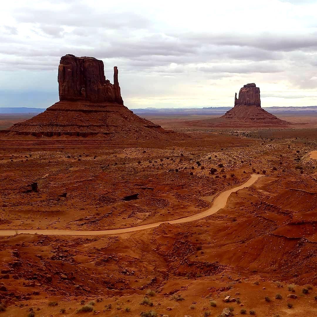 Two sandstone buttes in Monument Valley with a dirt road winding through the desert.
