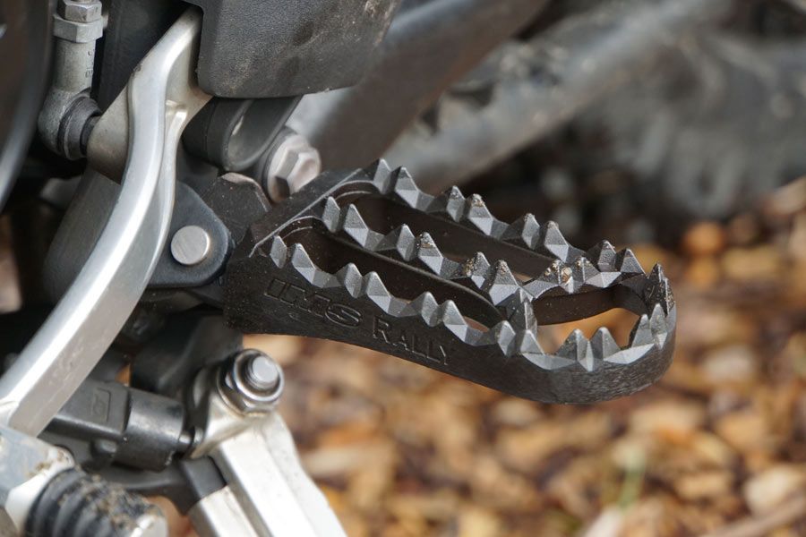 Black motorcycle foot peg with sharp teeth, attached to the frame.