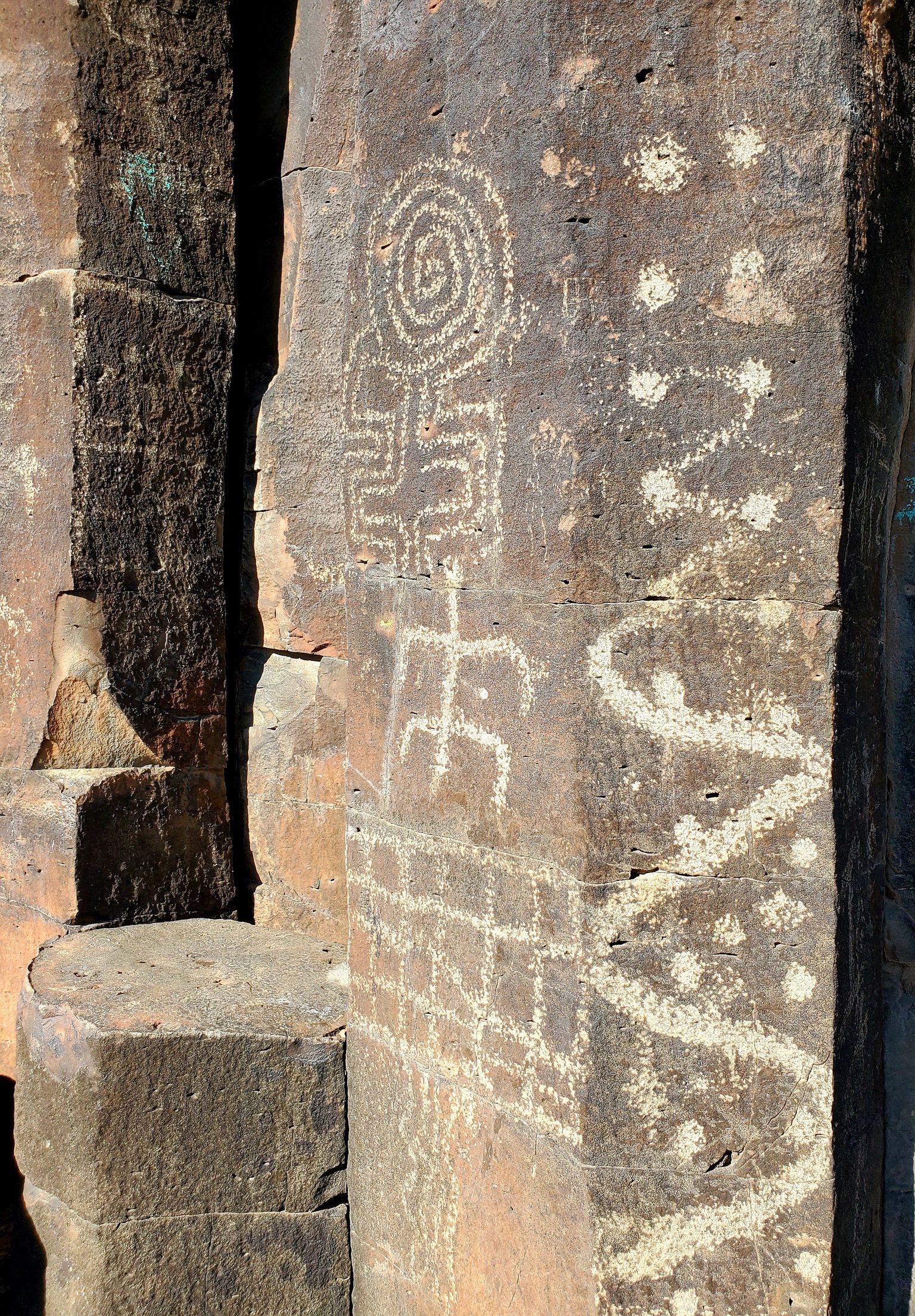 Close-up of rock wall with ancient petroglyphs; symbols, spirals, and lines etched into the surface.