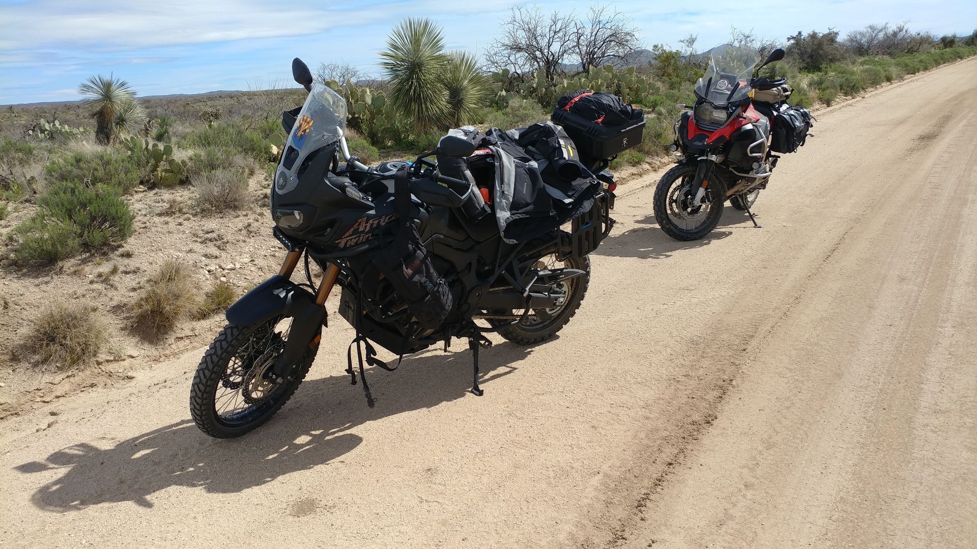 Two adventure motorcycles parked on a dirt road in a desert landscape.