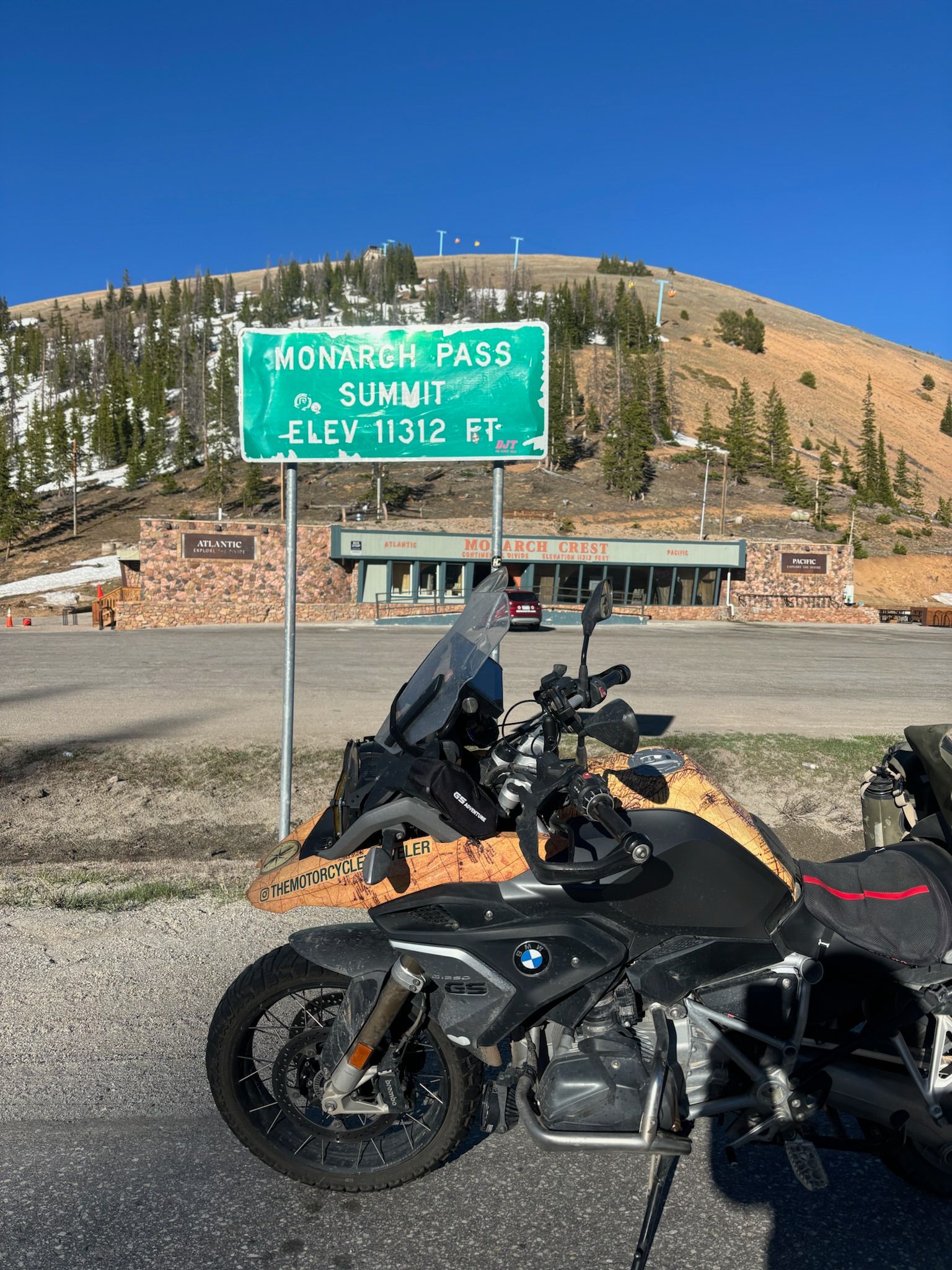 Motorcycle parked by a sign for Mount Rose Pass summit, elevation 10,712 ft. Mountains in background.