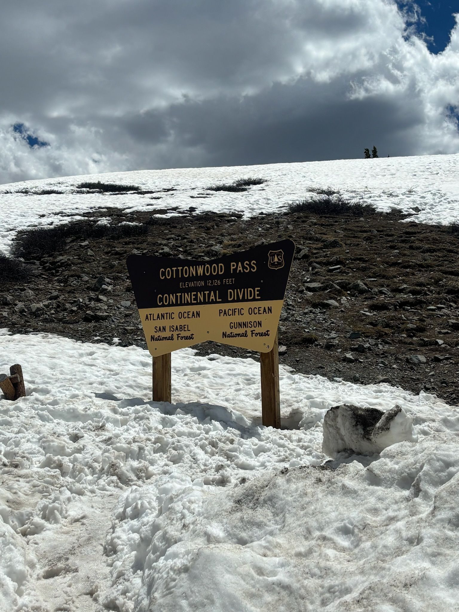 Sign on snowy mountain with text, Continental Divide sign. White snow, blue sky with clouds.